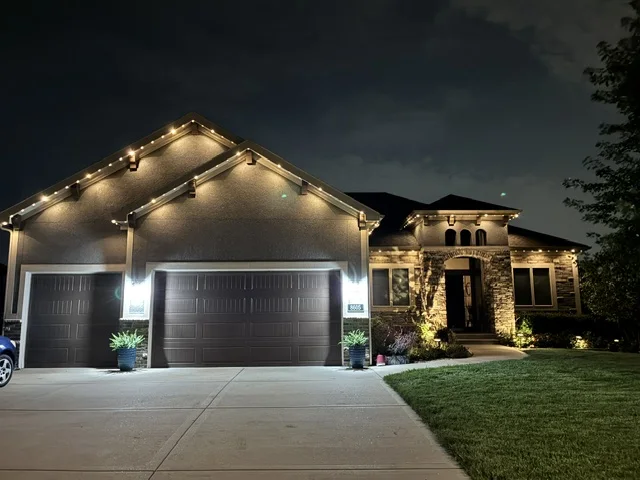 A completed permanent-lighting installation with warm-white roofline lights on a home with two garage doors